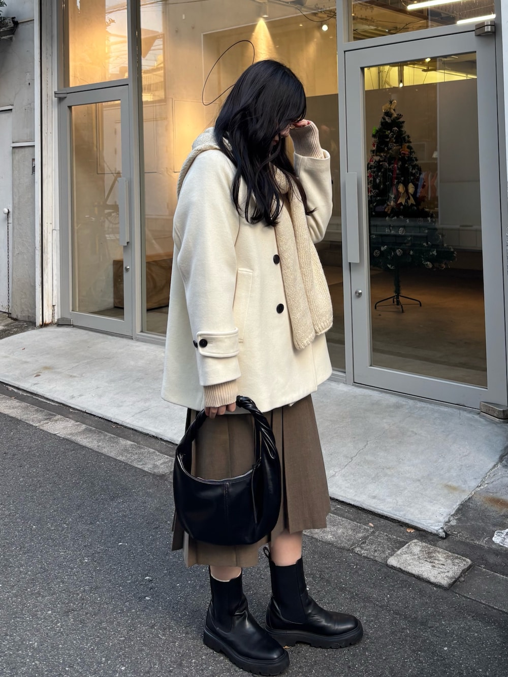 ホワイト系のピーコート、ブラウン系のスカート、ブラック系のハンドバッグを着用したレディースの冬コーディネートの2枚目の写真
