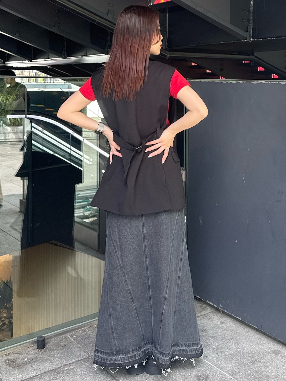 レッド系のTシャツ/カットソー、ブラック系のベスト、ブラック系のデニムスカートを着用したレディースの春コーディネートの3枚目の写真