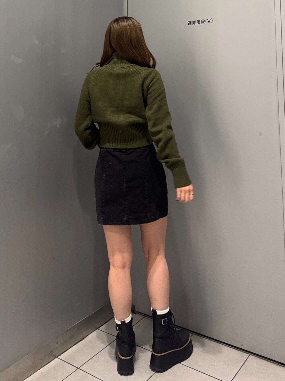 ブラック系のスカート、グリーン系のニット/セーター、ブラック系のブーツを着用したレディースの秋コーディネートの3枚目の写真