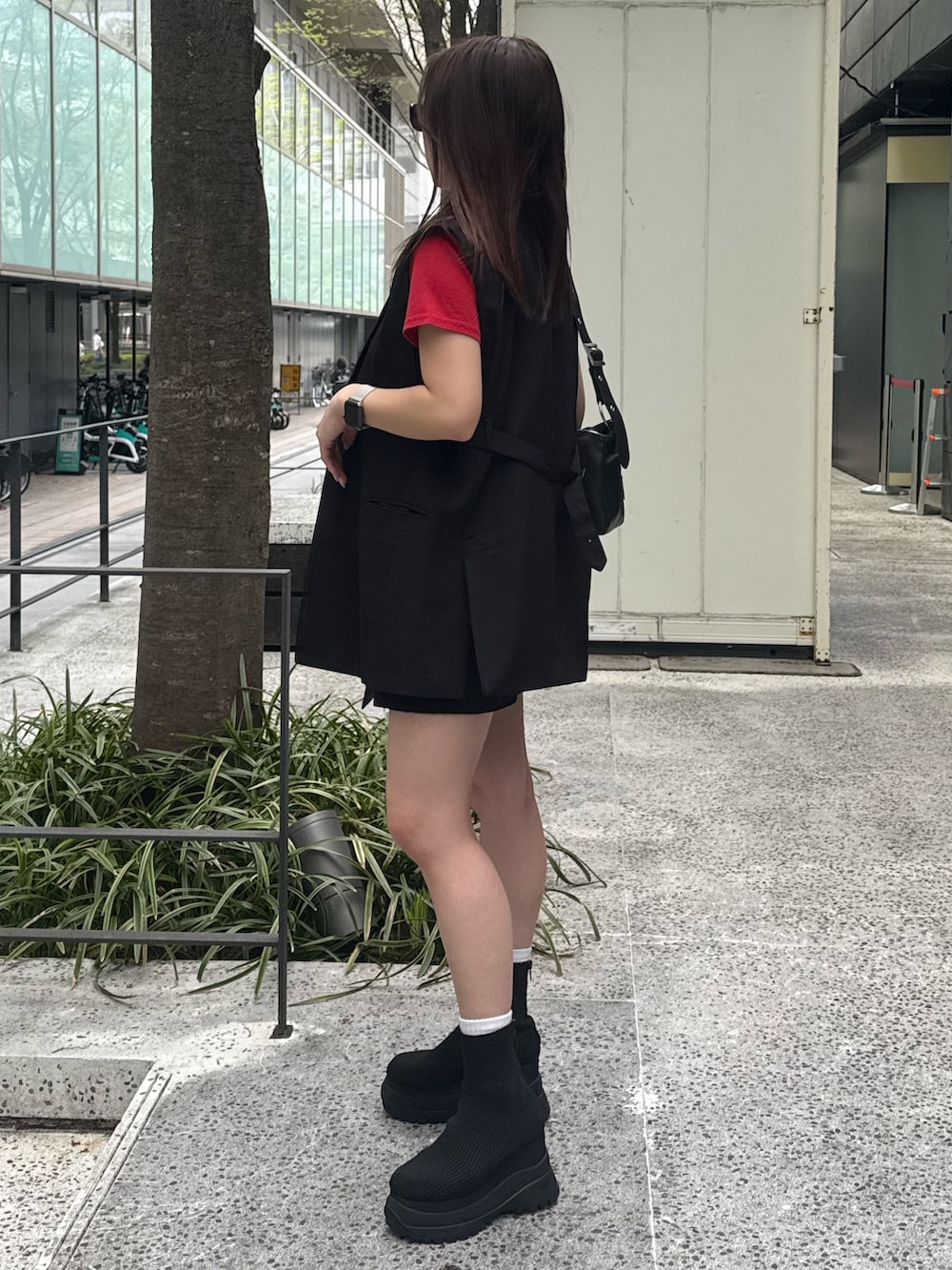 レッド系のTシャツ/カットソー、ブラック系のベスト、ブラック系のスカートを着用したレディースの春コーディネートの2枚目の写真