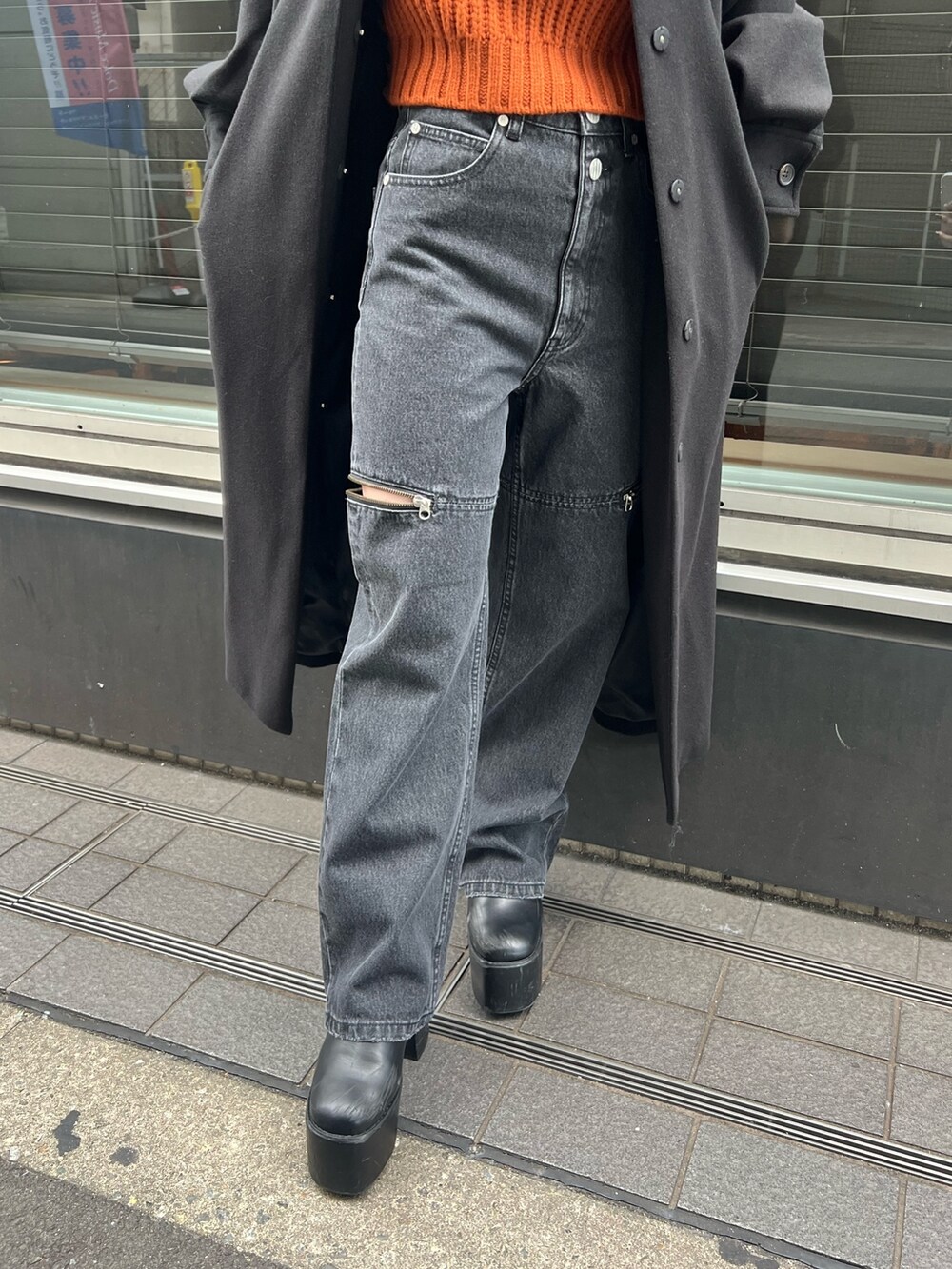ブラック系のデニムパンツ、オレンジ系のニット/セーター、ブラック系のステンカラーコートを着用したレディースの秋コーディネートの6枚目の写真