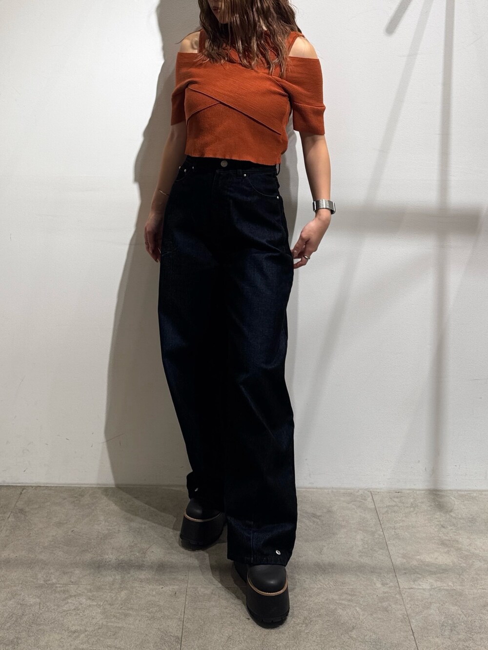 オレンジ系のニット/セーター、ブラック系のデニムパンツ、ブラック系のブーツを着用したレディースの夏コーディネートの4枚目の写真