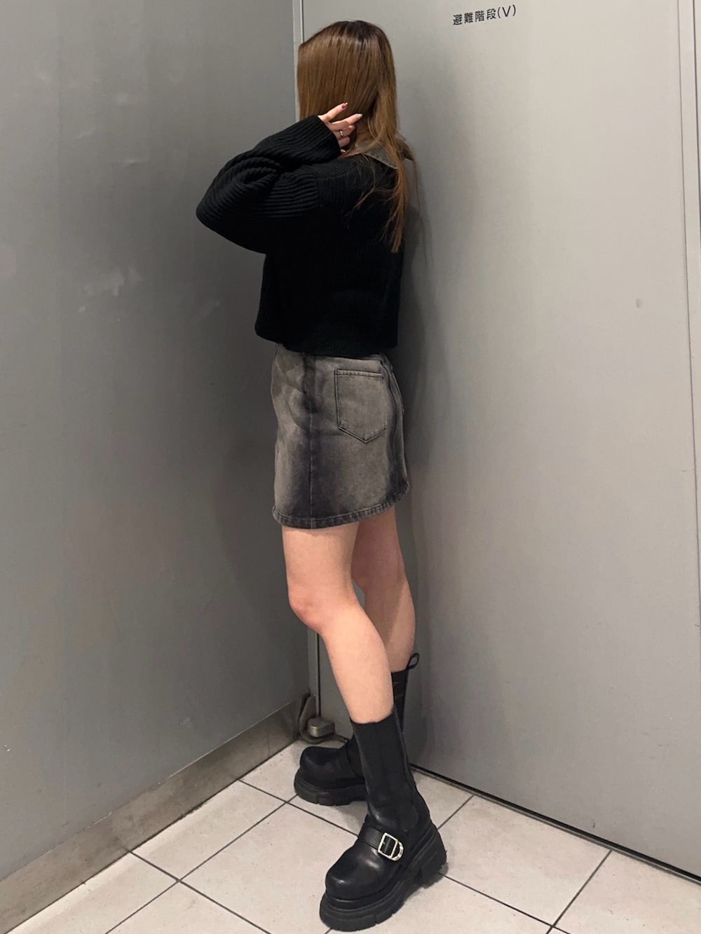 ブラック系のデニムスカート、ブラック系のニット/セーター、ブラック系のブーツを着用したレディースの冬コーディネートの2枚目の写真