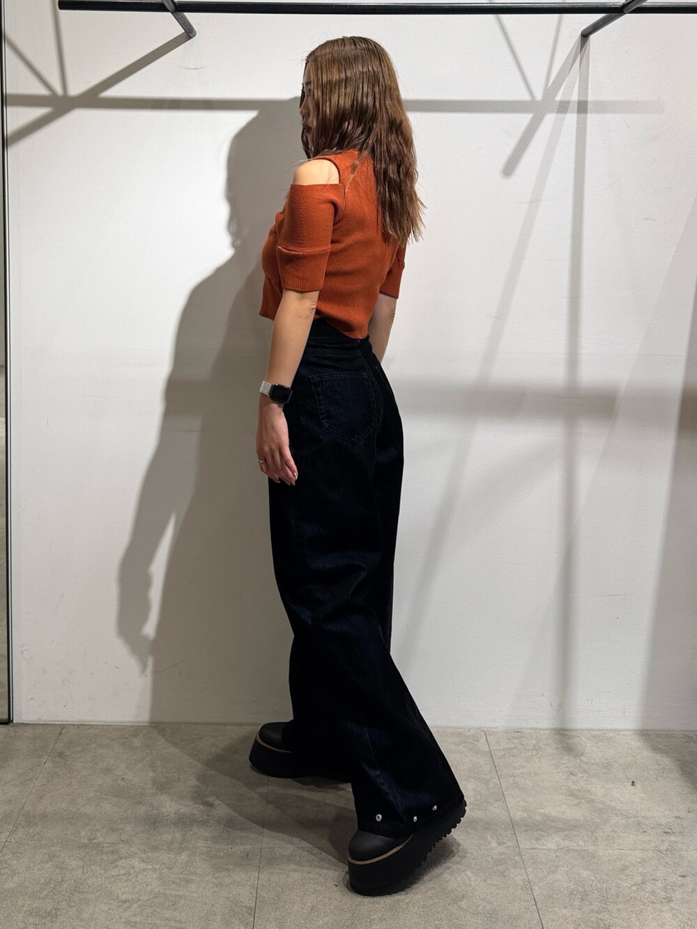 オレンジ系のニット/セーター、ブラック系のデニムパンツ、ブラック系のブーツを着用したレディースの夏コーディネートの2枚目の写真