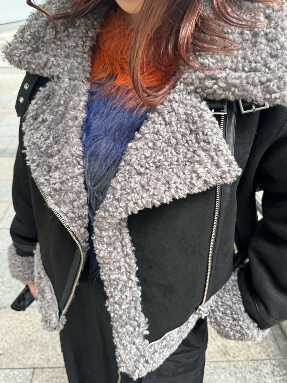 ブラック系のムートンコート、オレンジ系のニット/セーター、ブラック系のスカートを着用したレディースの冬コーディネートの5枚目の写真