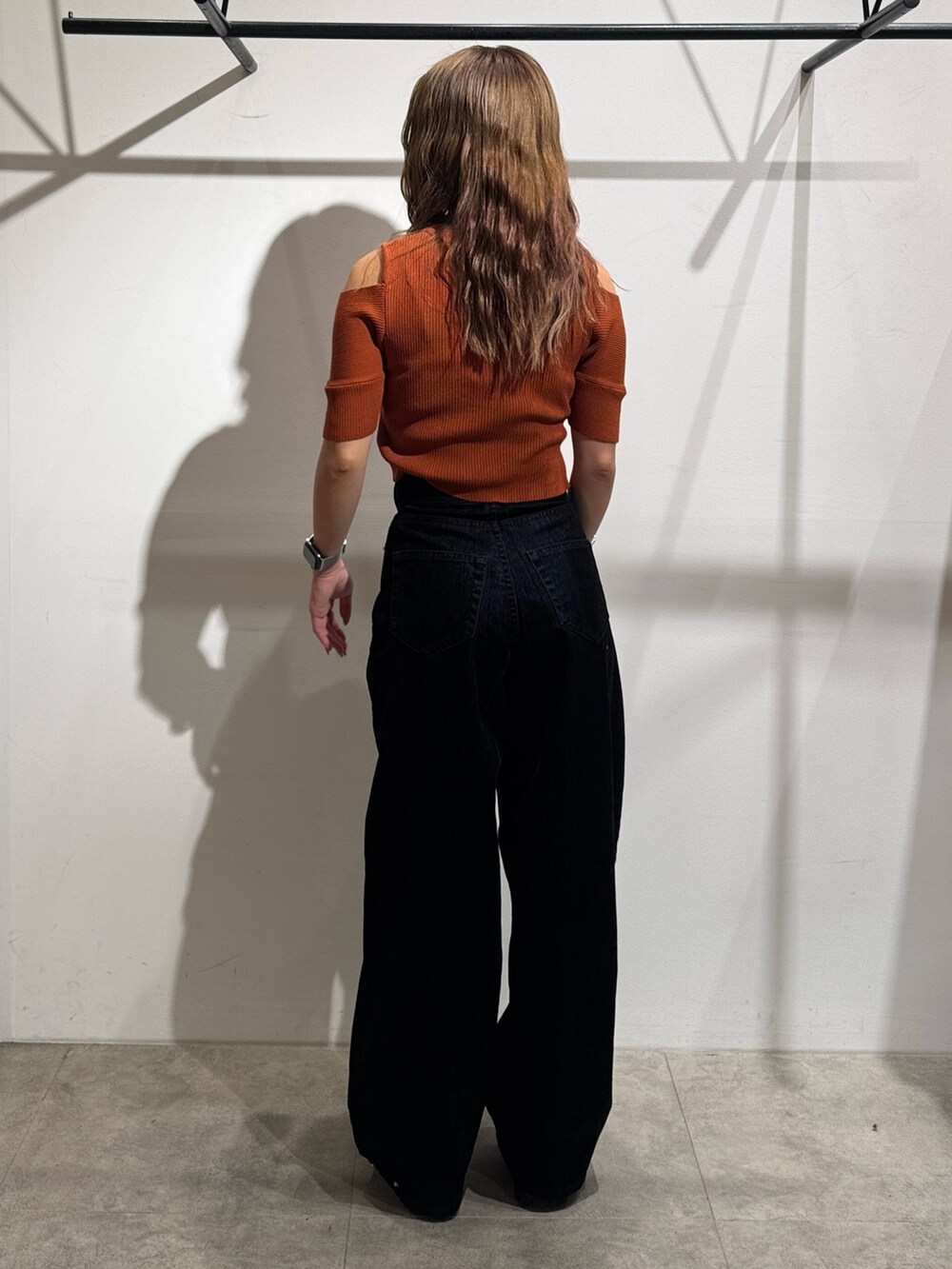 オレンジ系のニット/セーター、ブラック系のデニムパンツ、ブラック系のブーツを着用したレディースの夏コーディネートの3枚目の写真