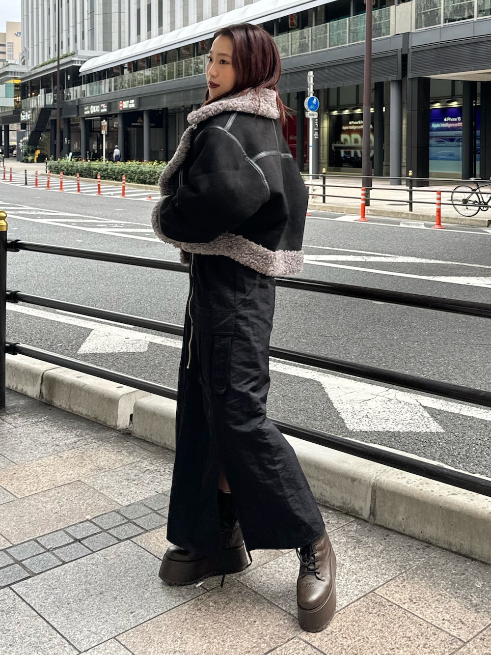 ブラック系のムートンコート、オレンジ系のニット/セーター、ブラック系のスカートを着用したレディースの冬コーディネートの2枚目の写真