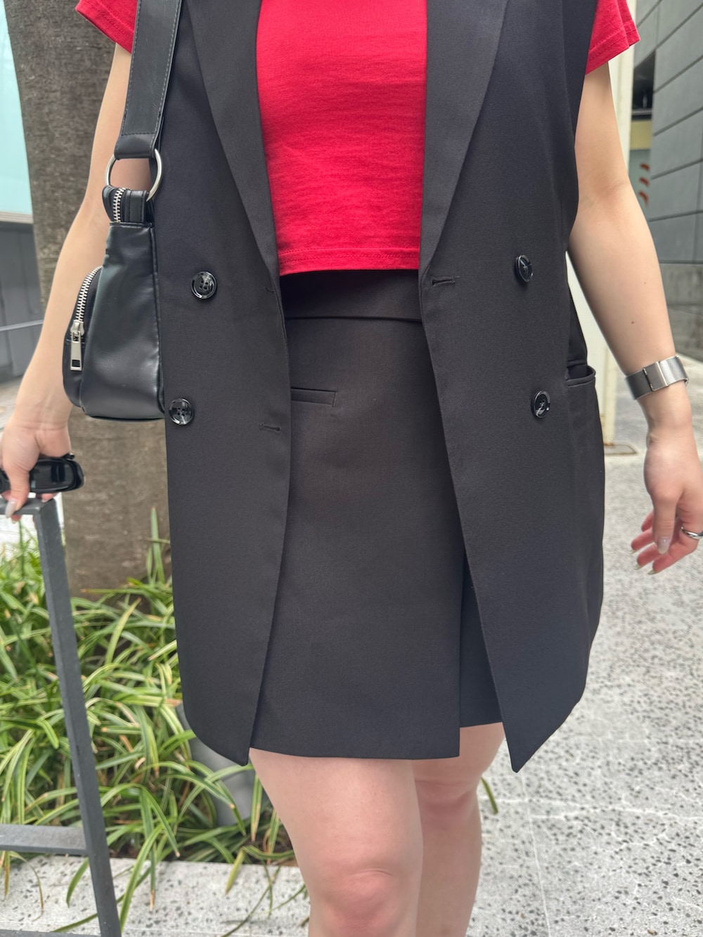 レッド系のTシャツ/カットソー、ブラック系のベスト、ブラック系のスカートを着用したレディースの春コーディネートの6枚目の写真