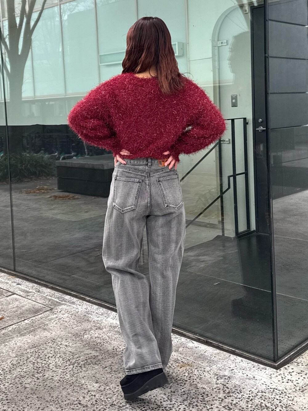 レッド系のニット/セーター、ブラック系のデニムパンツ、ブラック系のブーツを着用したレディースの冬コーディネートの3枚目の写真