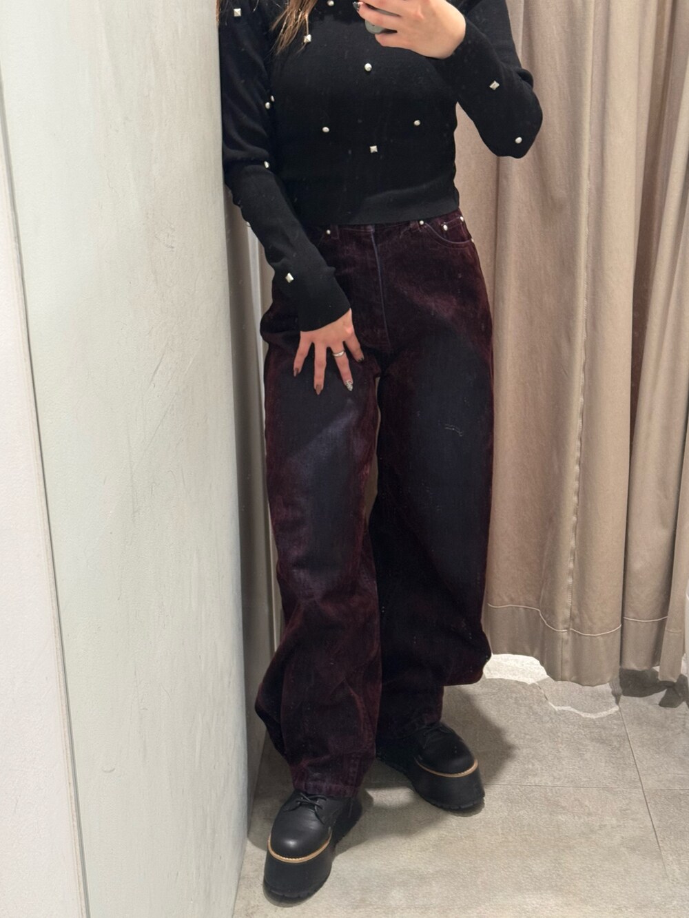レッド系のデニムパンツ、ブラック系のニット/セーター、ブラック系のブーツを着用したレディースの秋コーディネートの5枚目の写真