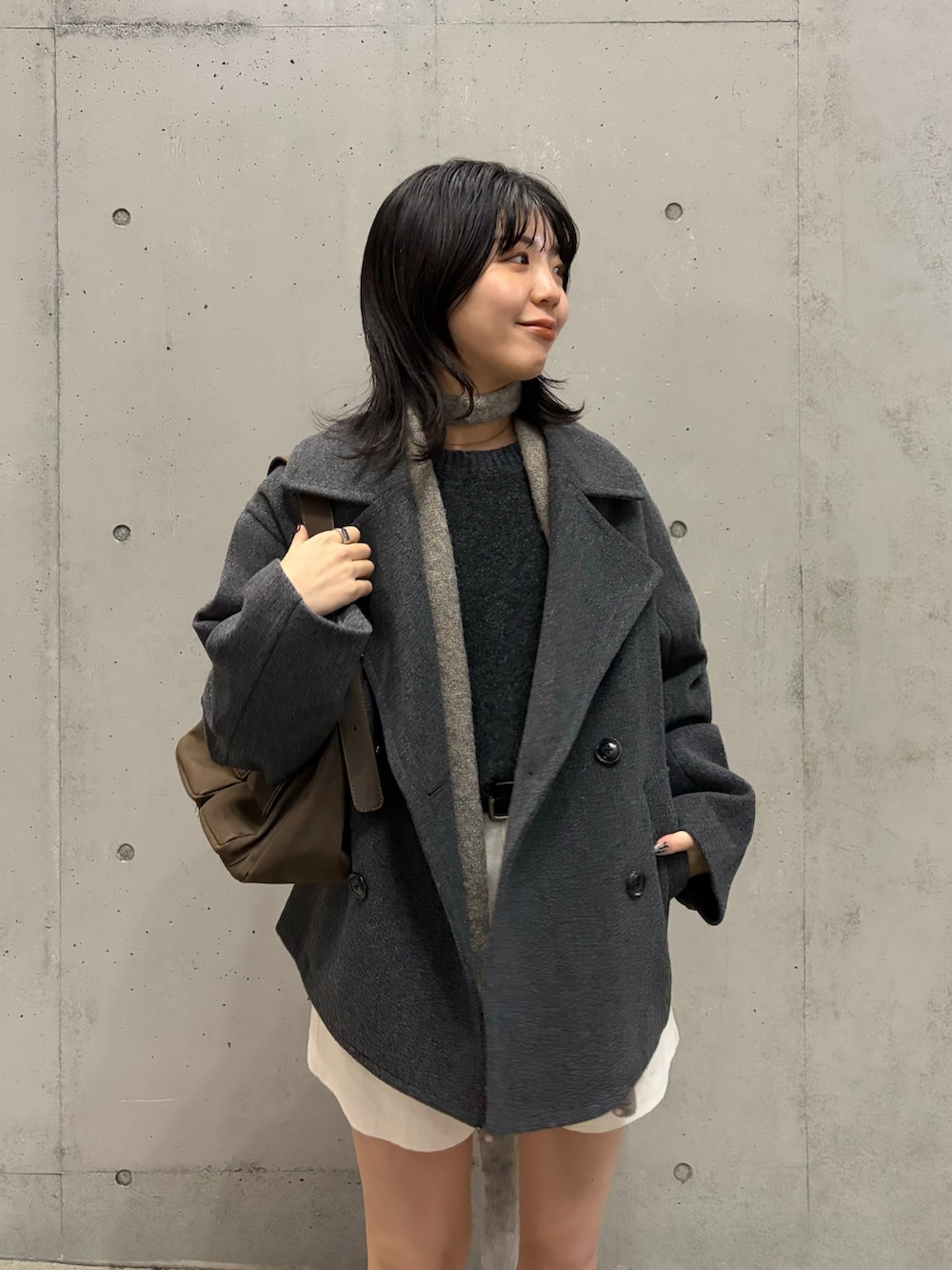 グレー系のピーコート、ブラウン系のショルダーバッグ、グレー系のニット/セーターを着用したレディースの冬コーディネートの3枚目の写真