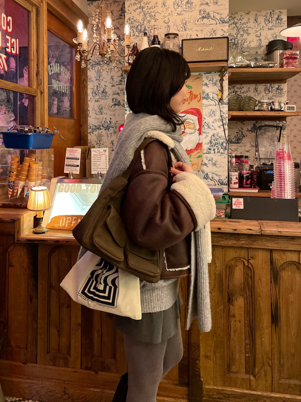 ブラウン系のムートンコート、グレー系のニット/セーター、ブラウン系のショルダーバッグを着用したレディースの冬コーディネートの2枚目の写真