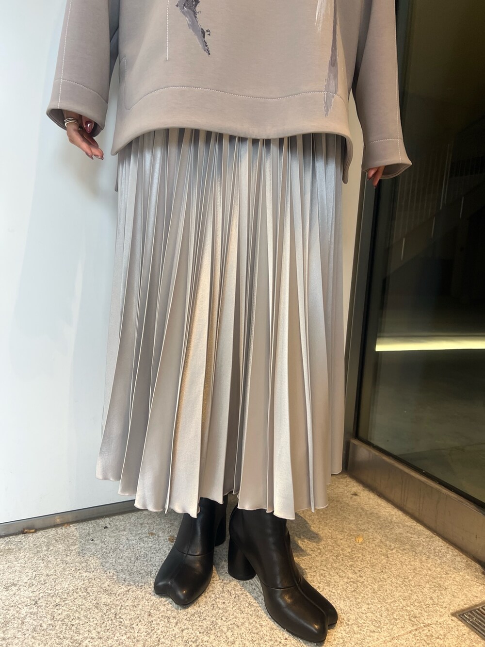 シルバー系のスカート、ベージュ系のTシャツ/カットソー、ブラック系のブーツを着用したレディースの冬コーディネートの7枚目の写真