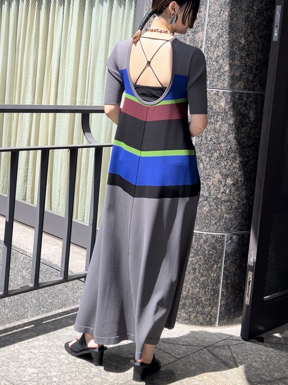 グレー系のワンピース、ブラック系のサンダル、シルバー系のネックレスを着用したレディースの春コーディネートの2枚目の写真