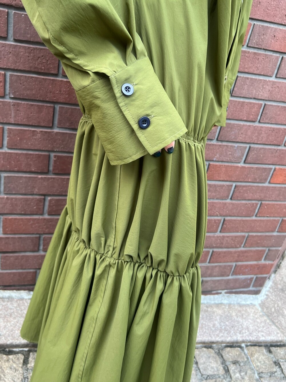 グリーン系のワンピース、ブラック系のブーツ、レッド系のイヤリングを着用したレディースの冬コーディネートの5枚目の写真