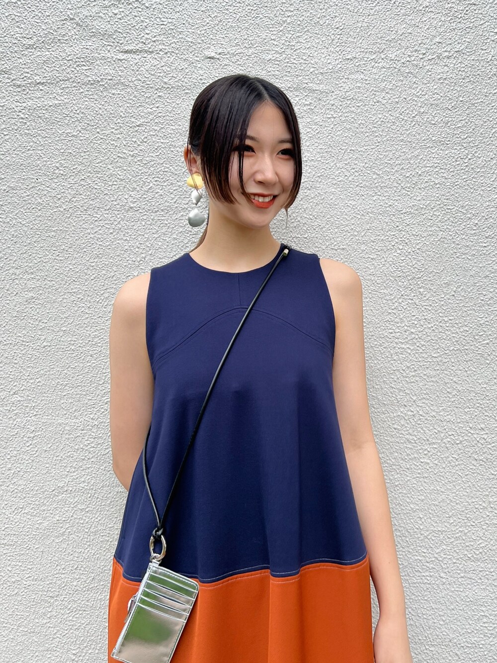 オレンジ系のワンピース、シルバー系の財布、シルバー系のイヤリングを着用したレディースの春コーディネートの4枚目の写真