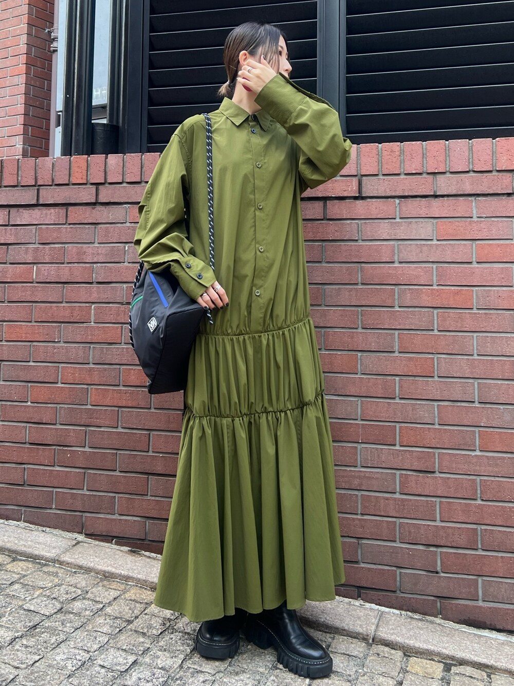 グリーン系のワンピース、ブラック系のブーツ、レッド系のイヤリングを着用したレディースの冬コーディネートの2枚目の写真