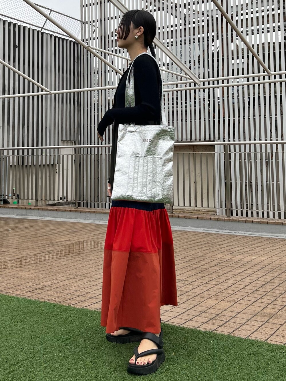 オレンジ系のワンピース、ブラック系のカーディガン/ボレロ、シルバー系のネックレスを着用したレディースの春コーディネートの2枚目の写真