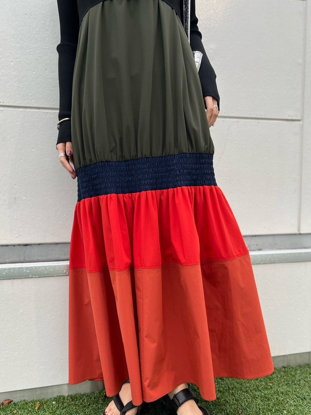 オレンジ系のワンピース、ブラック系のカーディガン/ボレロ、シルバー系のネックレスを着用したレディースの春コーディネートの8枚目の写真