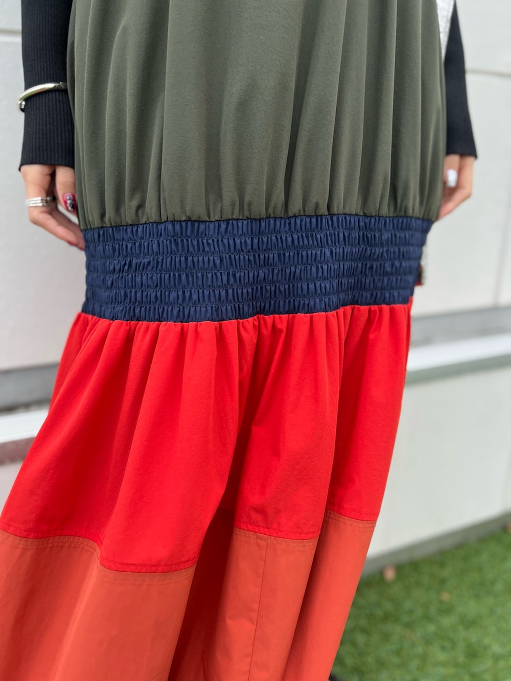 オレンジ系のワンピース、ブラック系のカーディガン/ボレロ、シルバー系のネックレスを着用したレディースの春コーディネートの6枚目の写真