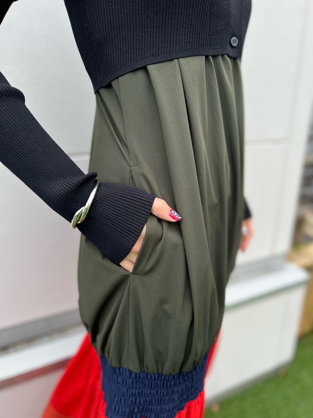 オレンジ系のワンピース、ブラック系のカーディガン/ボレロ、シルバー系のネックレスを着用したレディースの春コーディネートの7枚目の写真