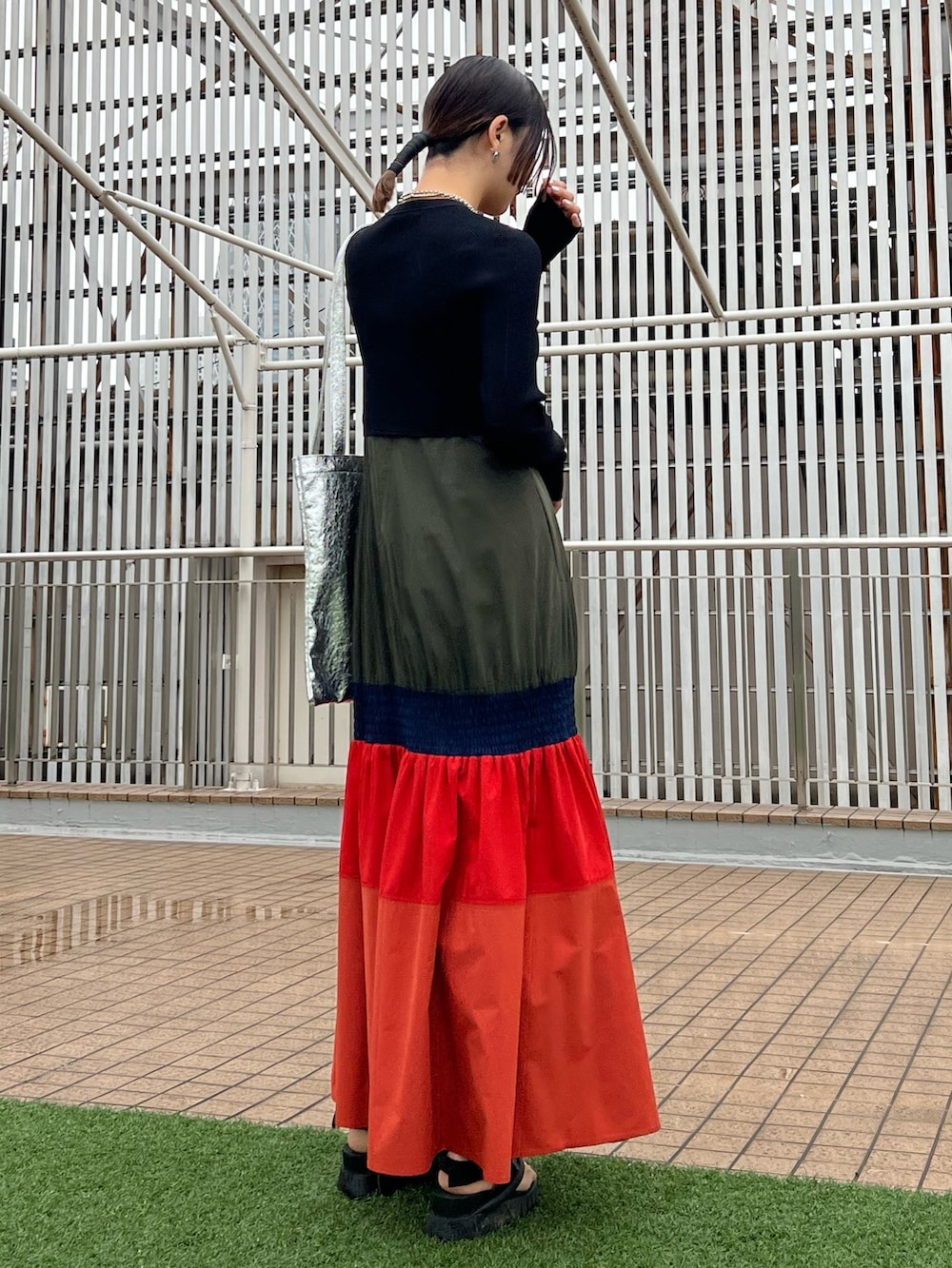 オレンジ系のワンピース、ブラック系のカーディガン/ボレロ、シルバー系のネックレスを着用したレディースの春コーディネートの3枚目の写真