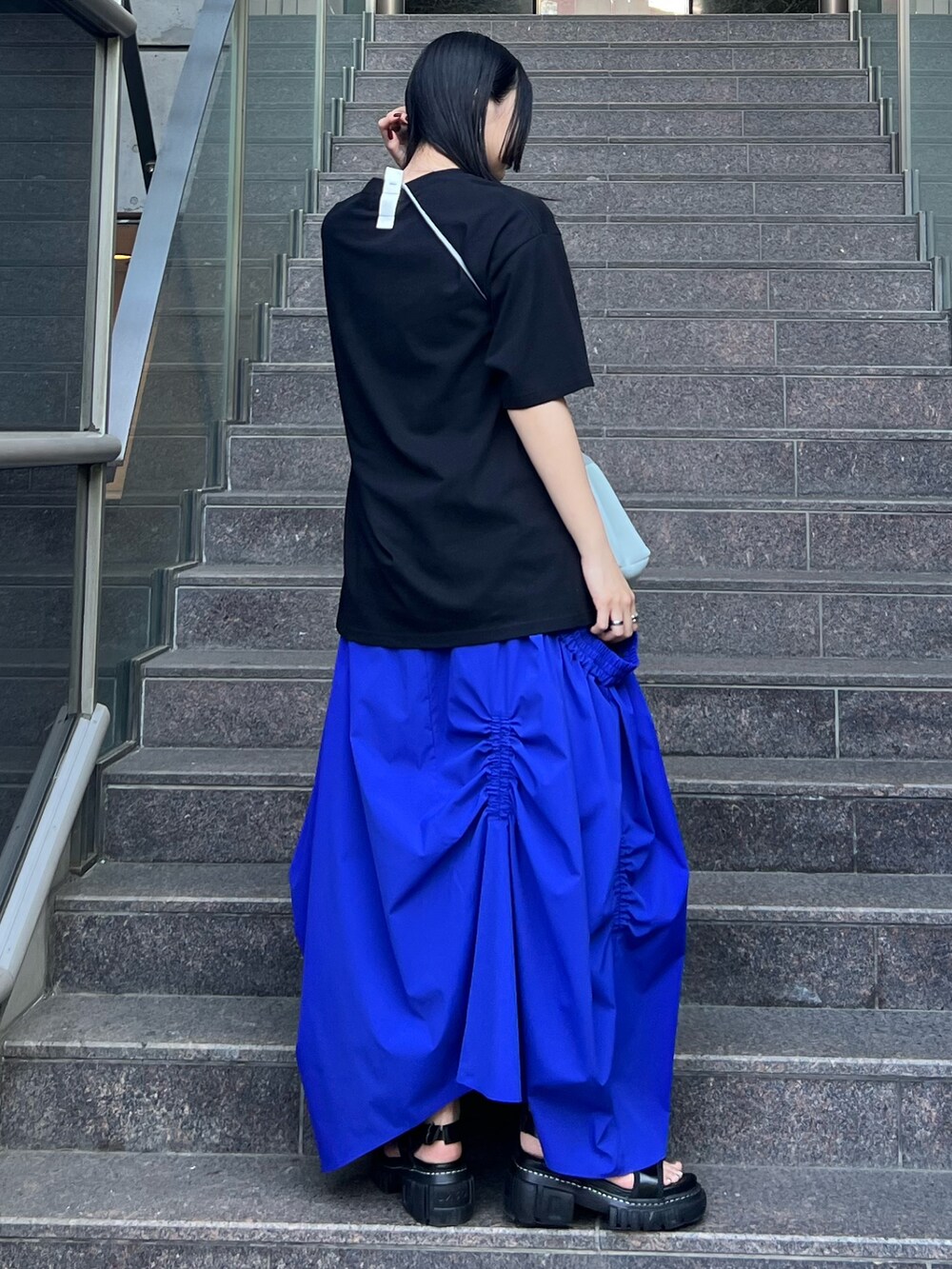 ブラック系のTシャツ/カットソー、ブルー系のスカート、グレー系のショルダーバッグを着用したレディースの夏コーディネートの2枚目の写真