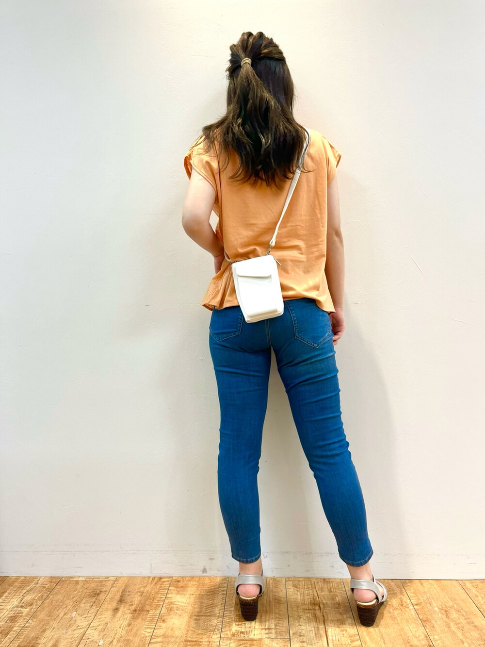 オレンジ系のTシャツ/カットソー、ブルー系のデニムパンツ、ホワイト系のショルダーバッグを着用したレディースの夏コーディネートの3枚目の写真