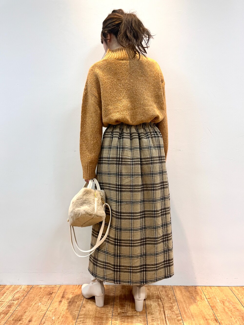 オレンジ系のニット/セーター、ベージュ系のスカート、ホワイト系のショルダーバッグを着用したレディースの冬コーディネートの3枚目の写真