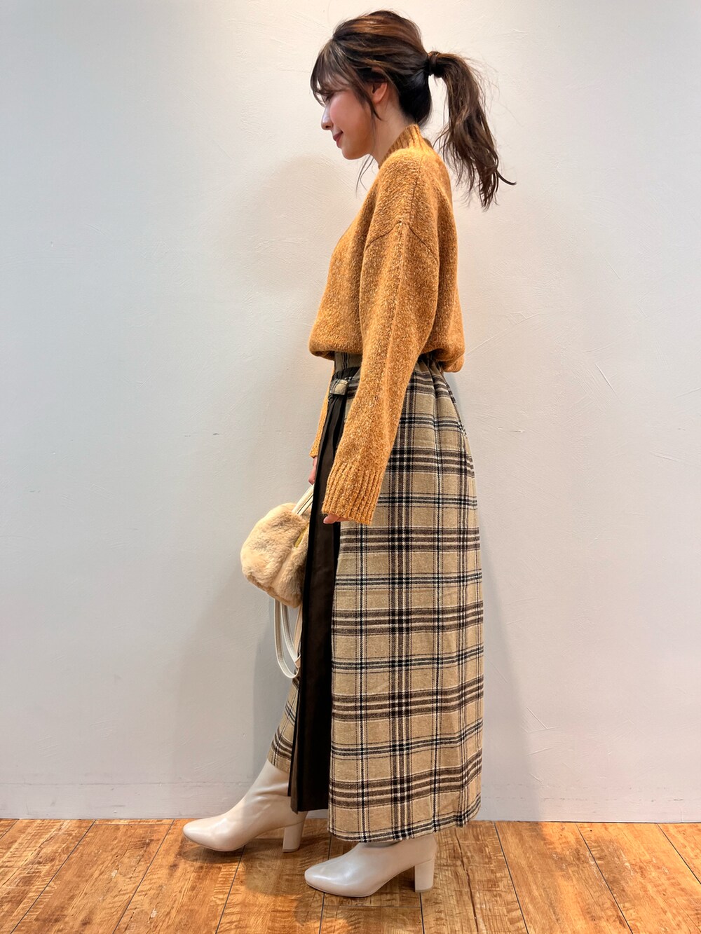 オレンジ系のニット/セーター、ベージュ系のスカート、ホワイト系のショルダーバッグを着用したレディースの冬コーディネートの2枚目の写真