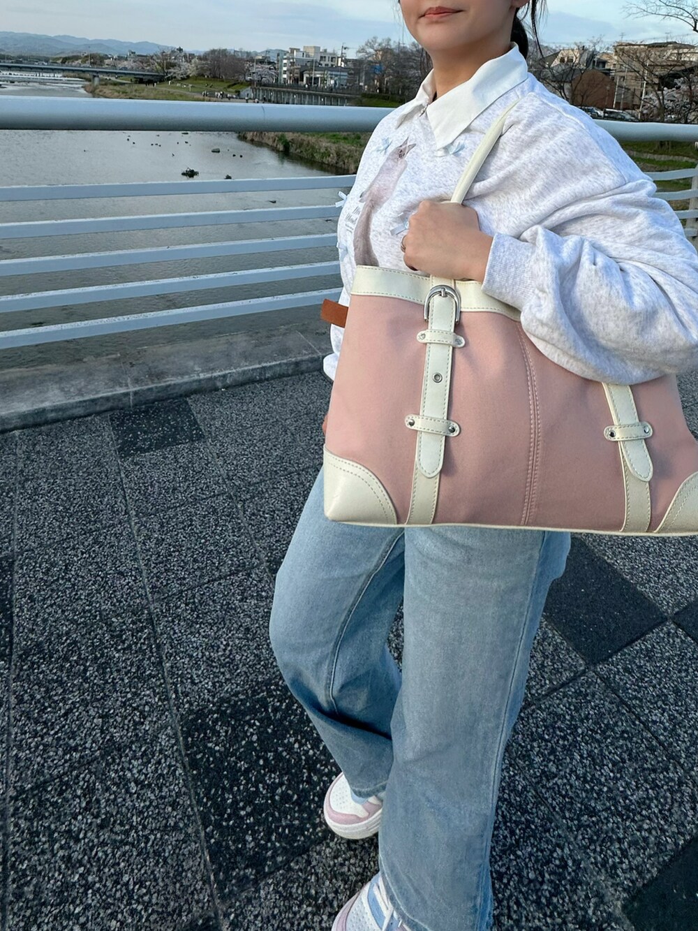 ホワイト系のスニーカー、ピンク系のショルダーバッグ、ブルー系のデニムパンツを着用したレディースの春コーディネートの2枚目の写真
