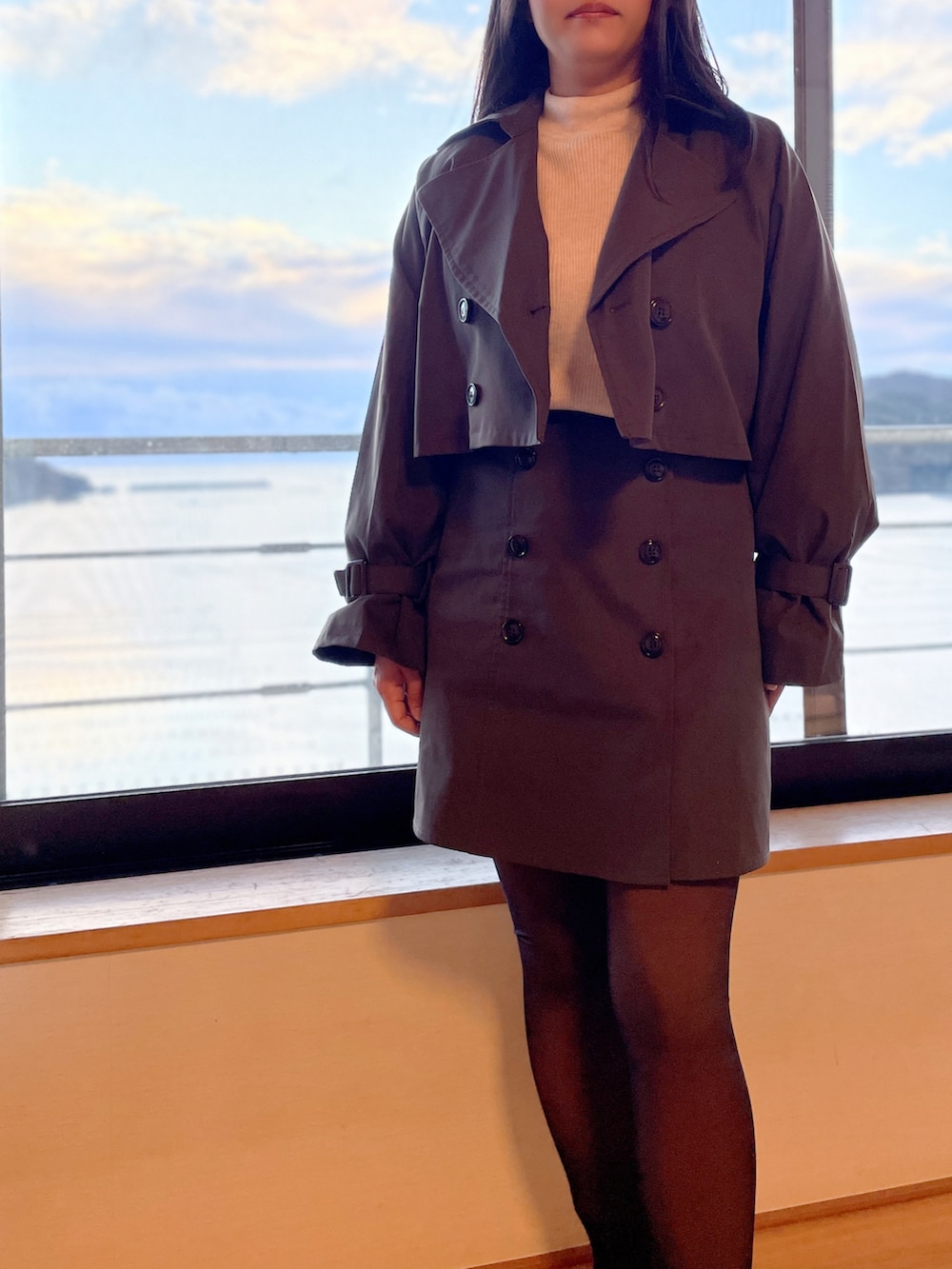 ホワイト系のニット/セーター、ブラウン系のトレンチコート、ブラウン系のスカートを着用したレディースの秋コーディネートの2枚目の写真