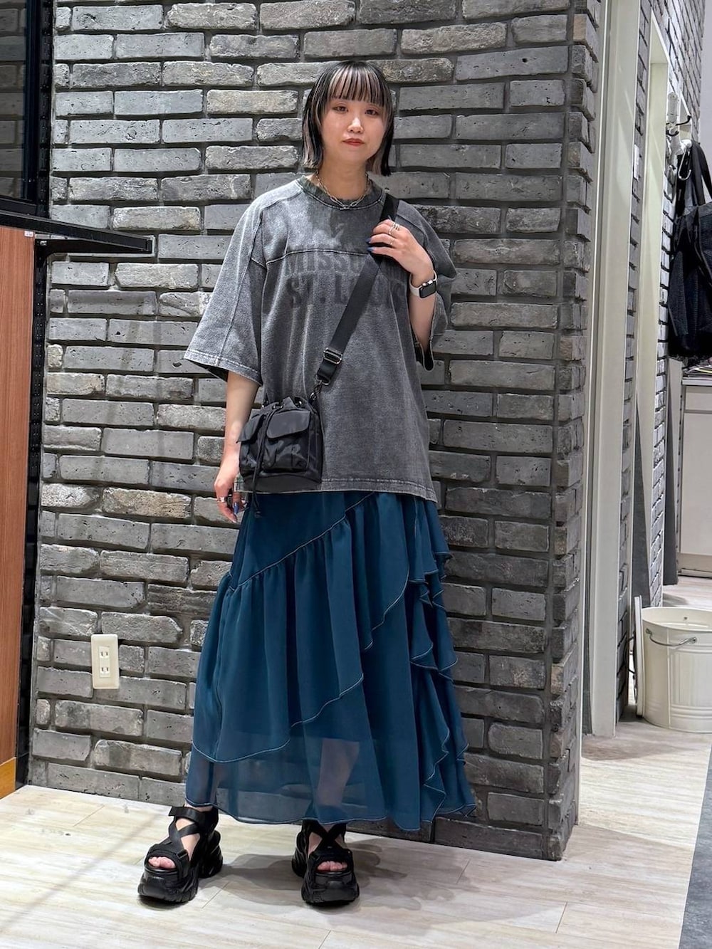 グリーン系のスカート、ブラック系のサンダル、ブラック系のショルダーバッグを着用したレディースの春コーディネートの2枚目の写真