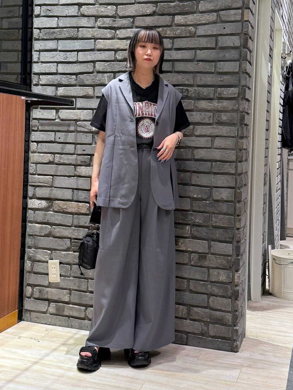 ブラック系のサンダル、ブラック系のショルダーバッグ、グレー系のスラックスを着用したレディースの春コーディネートの2枚目の写真