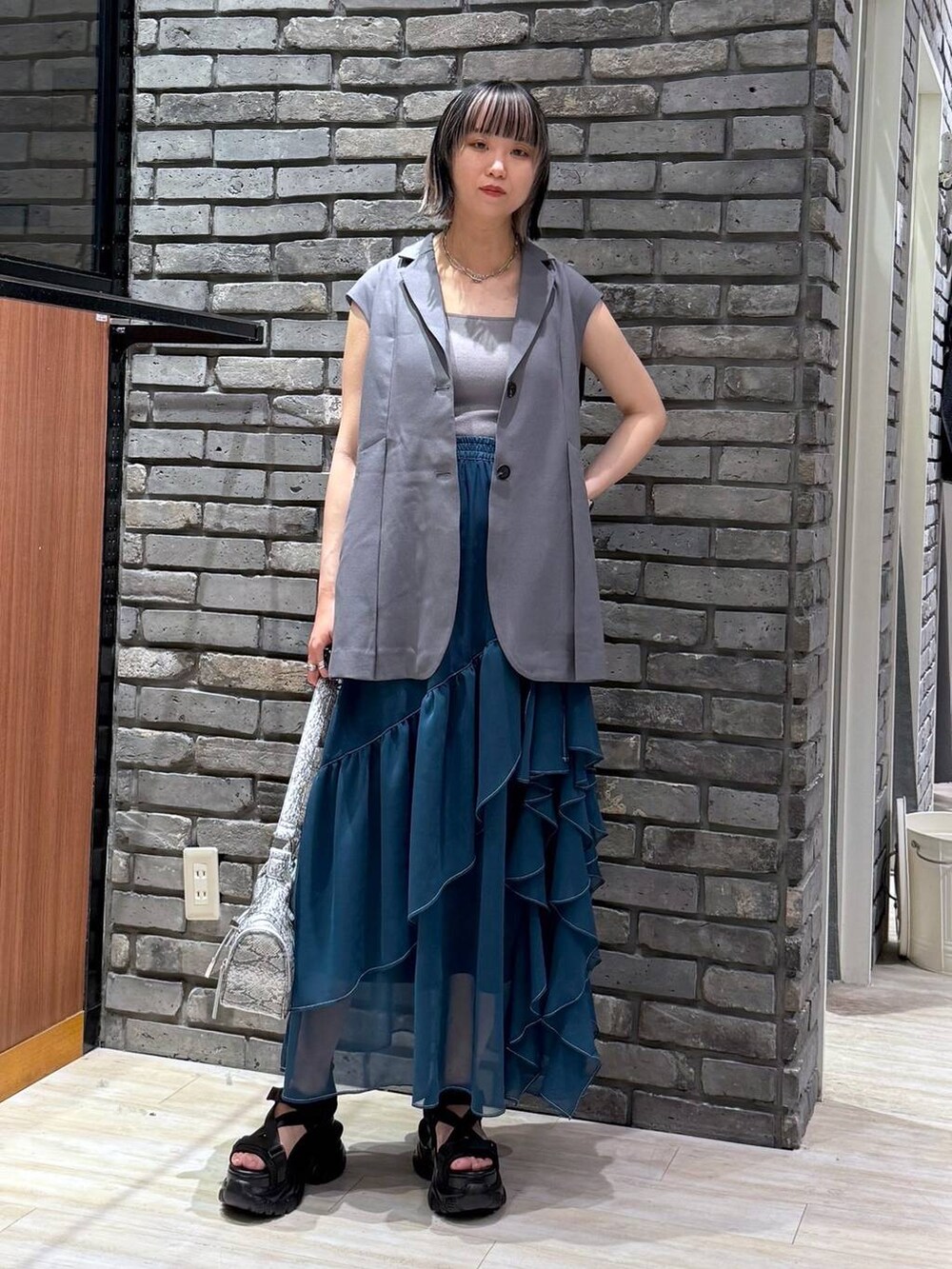 グリーン系のスカート、ブラック系のサンダル、ホワイト系のショルダーバッグを着用したレディースの春コーディネートの2枚目の写真