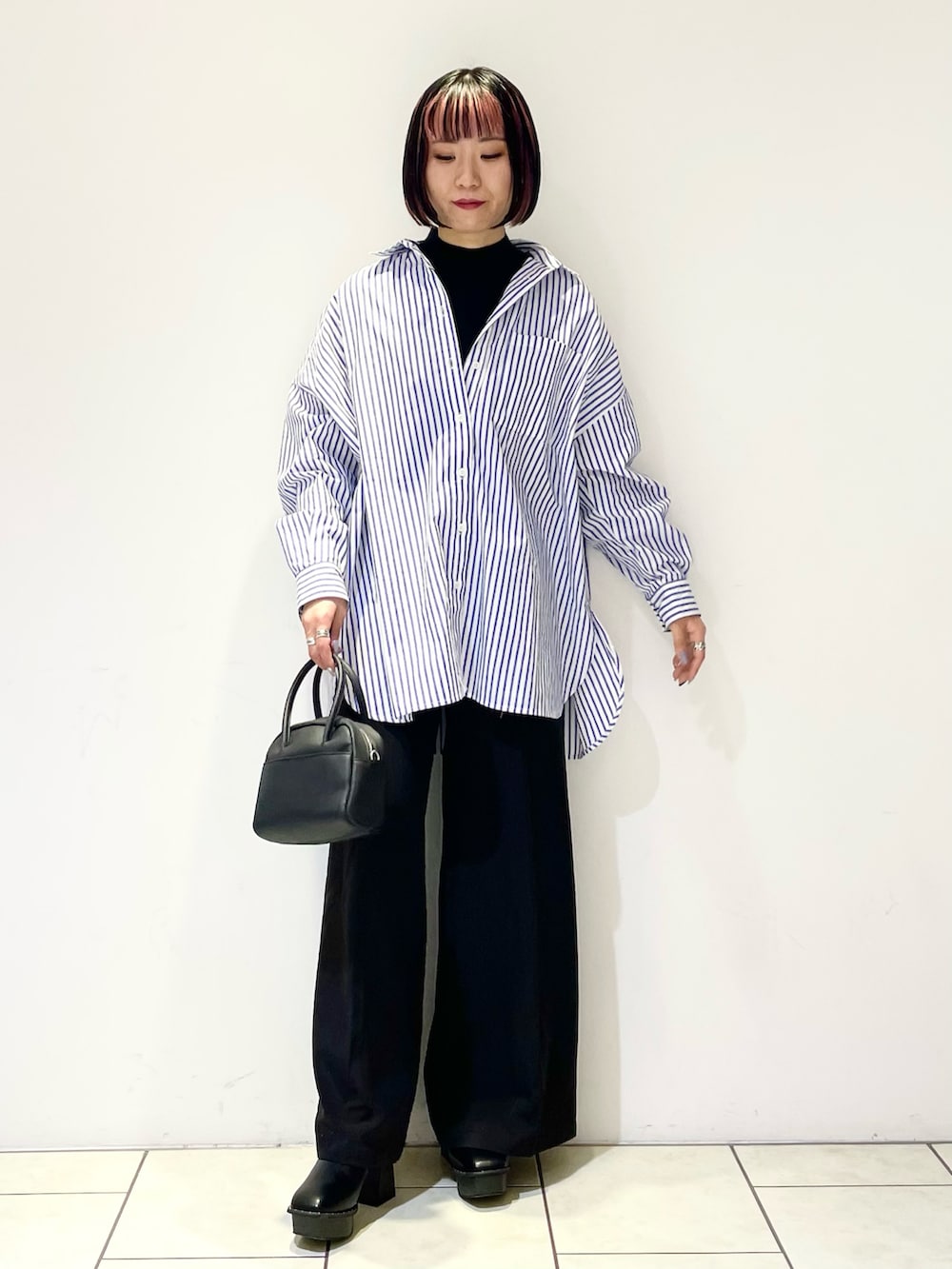 ブラック系のニット/セーター、ブルー系のシャツ/ブラウス、ブラック系のボストンバッグを着用したレディースの春コーディネートの2枚目の写真