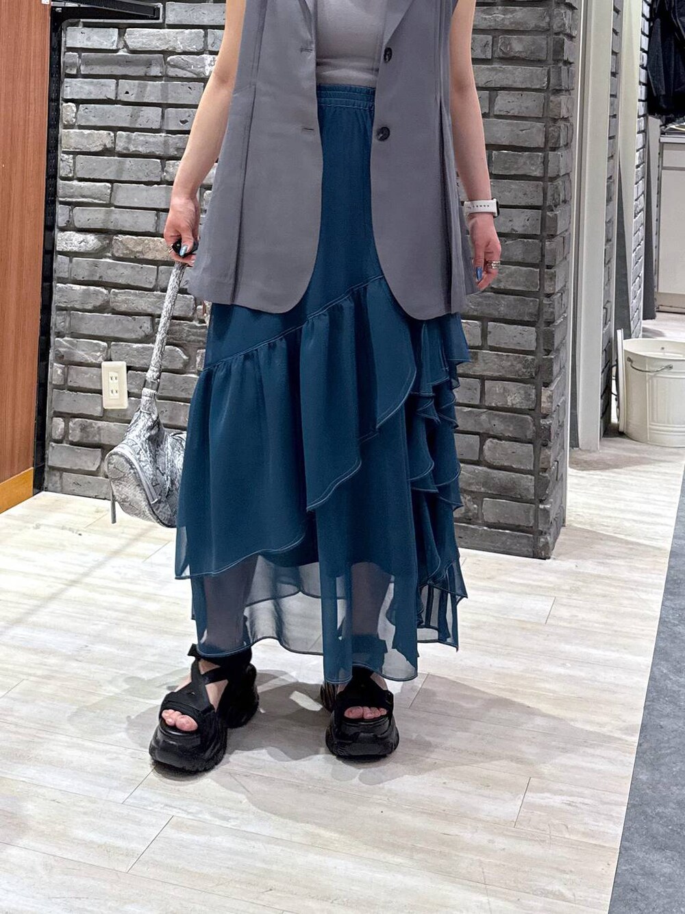 グリーン系のスカート、ブラック系のサンダル、ホワイト系のショルダーバッグを着用したレディースの春コーディネートの4枚目の写真