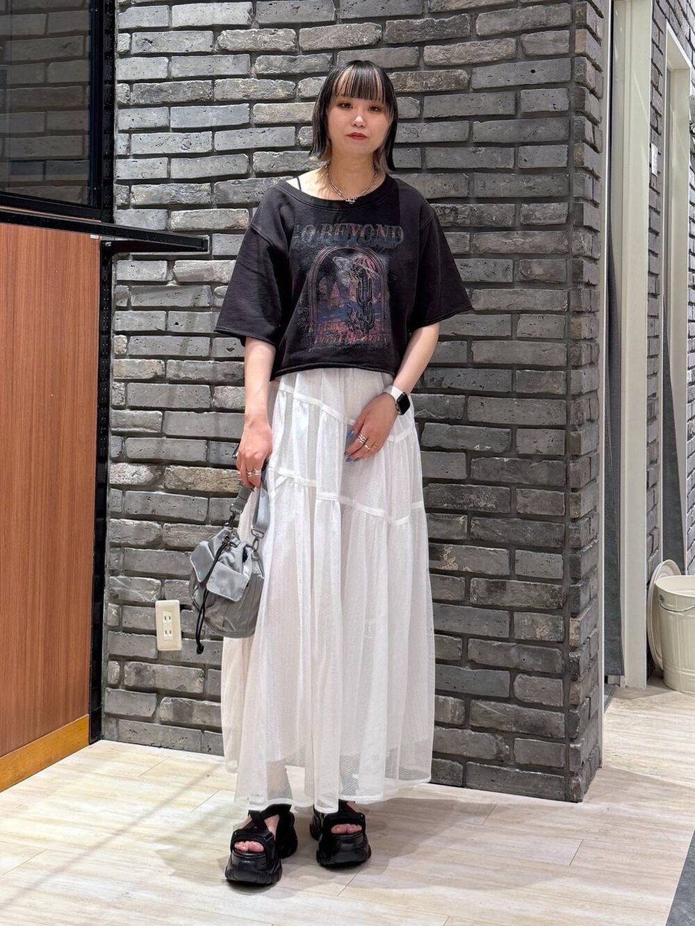 ブラック系のサンダル、ベージュ系のショルダーバッグ、グレー系のTシャツ/カットソーを着用したレディースの春コーディネートの2枚目の写真