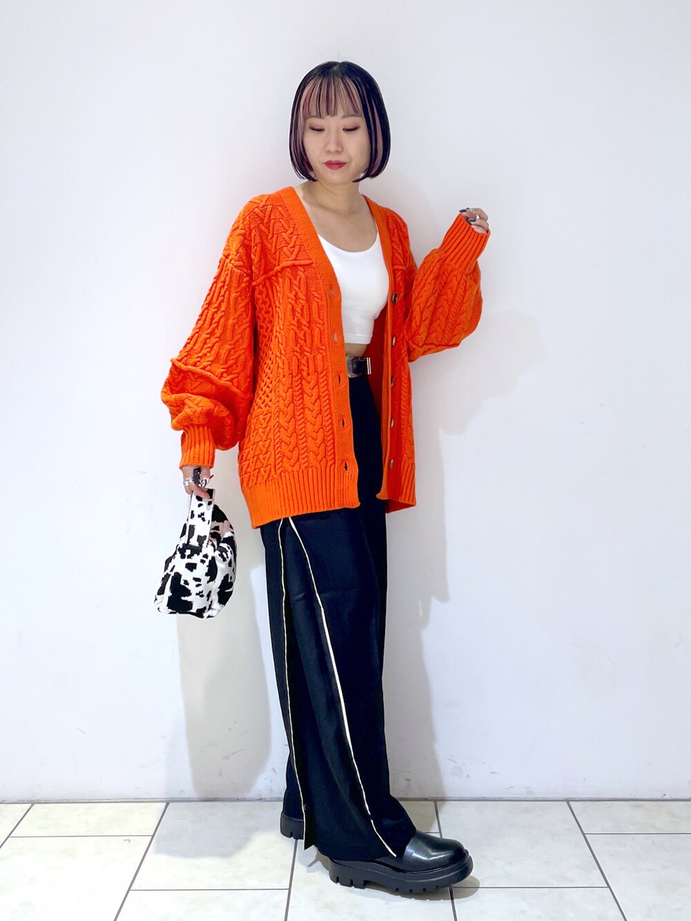 オレンジ系のカーディガン/ボレロ、ホワイト系のキャミソール、ブラック系のスラックスを着用したレディースの秋コーディネートの3枚目の写真