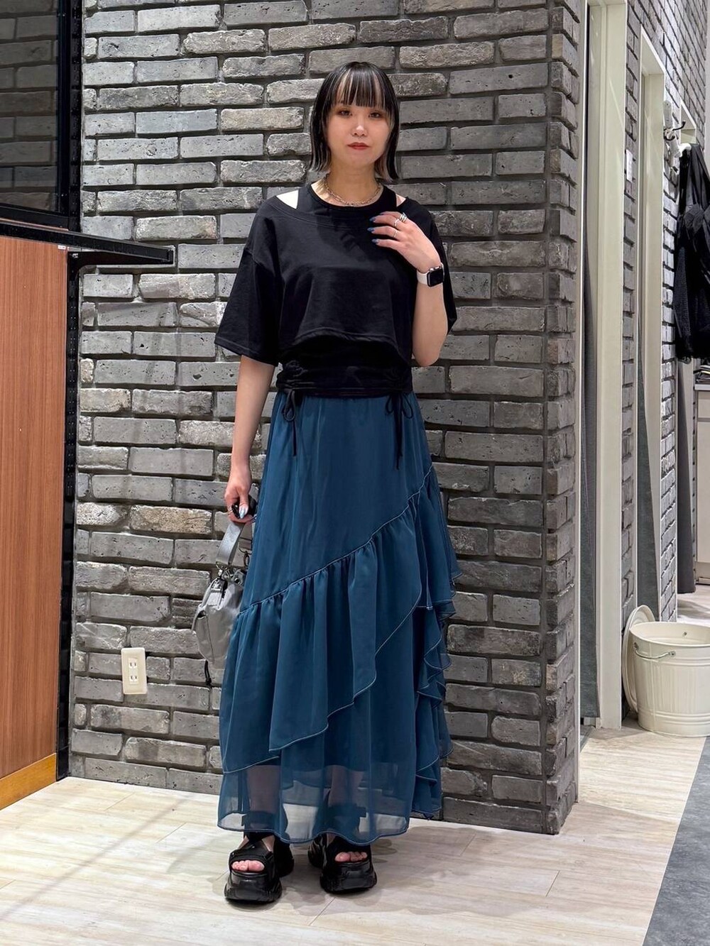 グリーン系のスカート、ブラック系のサンダル、ベージュ系のショルダーバッグを着用したレディースの春コーディネートの2枚目の写真