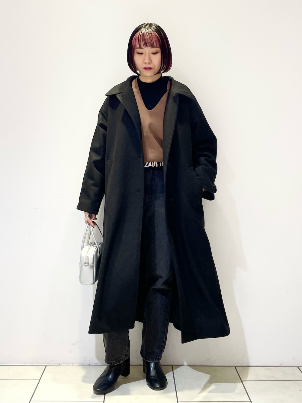 ブラック系のチェスターコート、ブラウン系のニット/セーター、ブラック系のニット/セーターを着用したレディースの春コーディネートの2枚目の写真