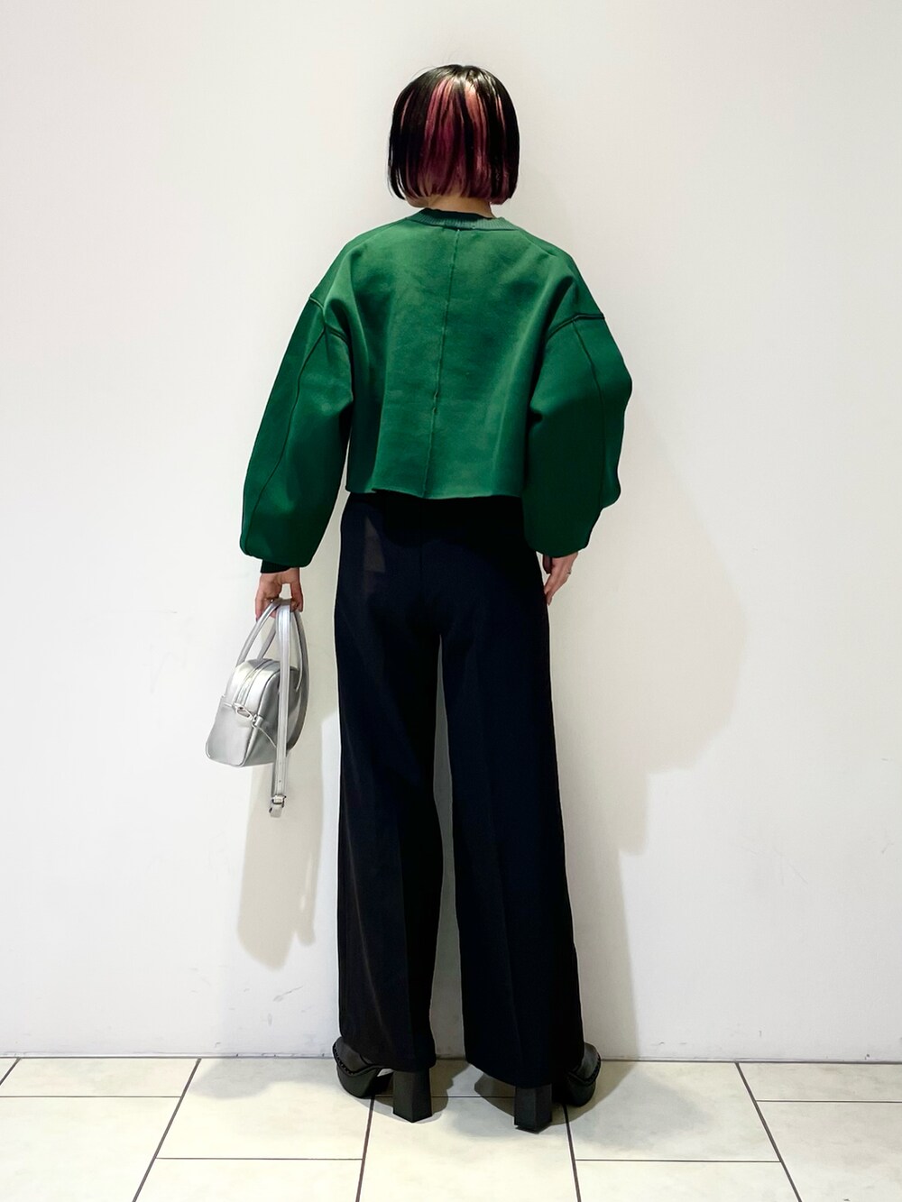 グリーン系のニット/セーター、シルバー系のボストンバッグ、ブラック系のスラックスを着用したレディースの春コーディネートの4枚目の写真