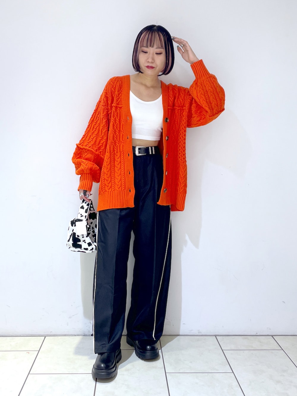 オレンジ系のカーディガン/ボレロ、ホワイト系のキャミソール、ブラック系のスラックスを着用したレディースの秋コーディネートの2枚目の写真