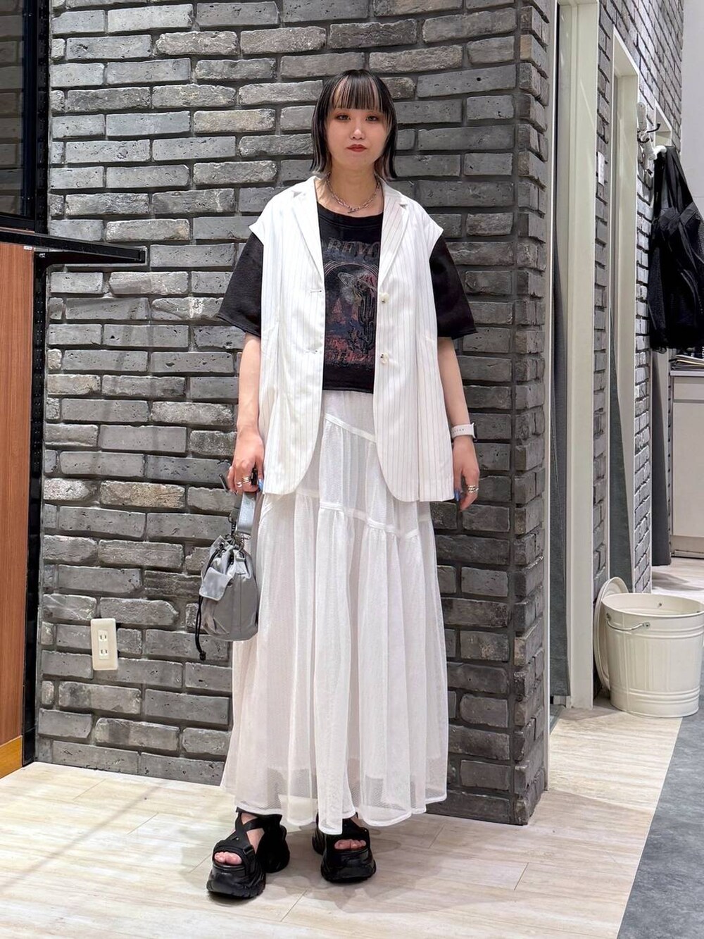 ブラック系のサンダル、ベージュ系のショルダーバッグ、ホワイト系のベストを着用したレディースの春コーディネートの2枚目の写真