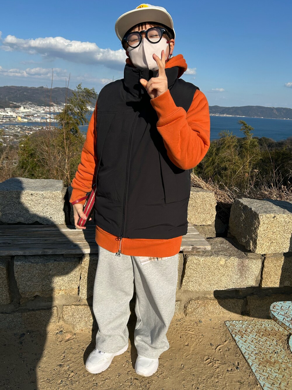 ブラック系のダウンベスト、オレンジ系のパーカー、グレー系のスウェットパンツを着用したレディースの冬コーディネートの2枚目の写真