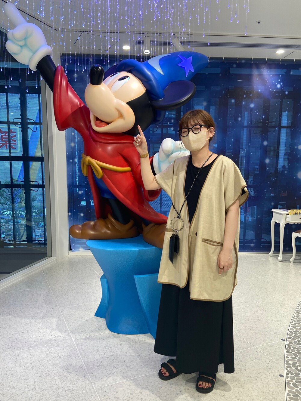 ブラック系のワンピース、ブラック系のサンダル、ベージュ系のベストを着用したレディースの夏コーディネートの2枚目の写真