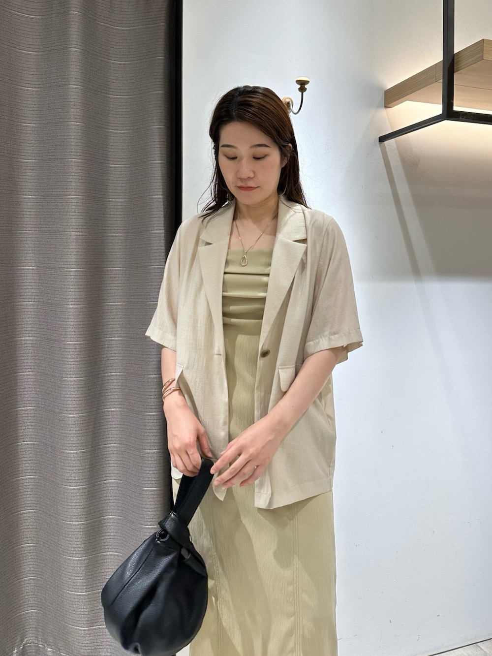 ホワイト系のテーラードジャケット、ベージュ系のワンピース、ブラック系のハンドバッグを着用したレディースの夏コーディネートの3枚目の写真