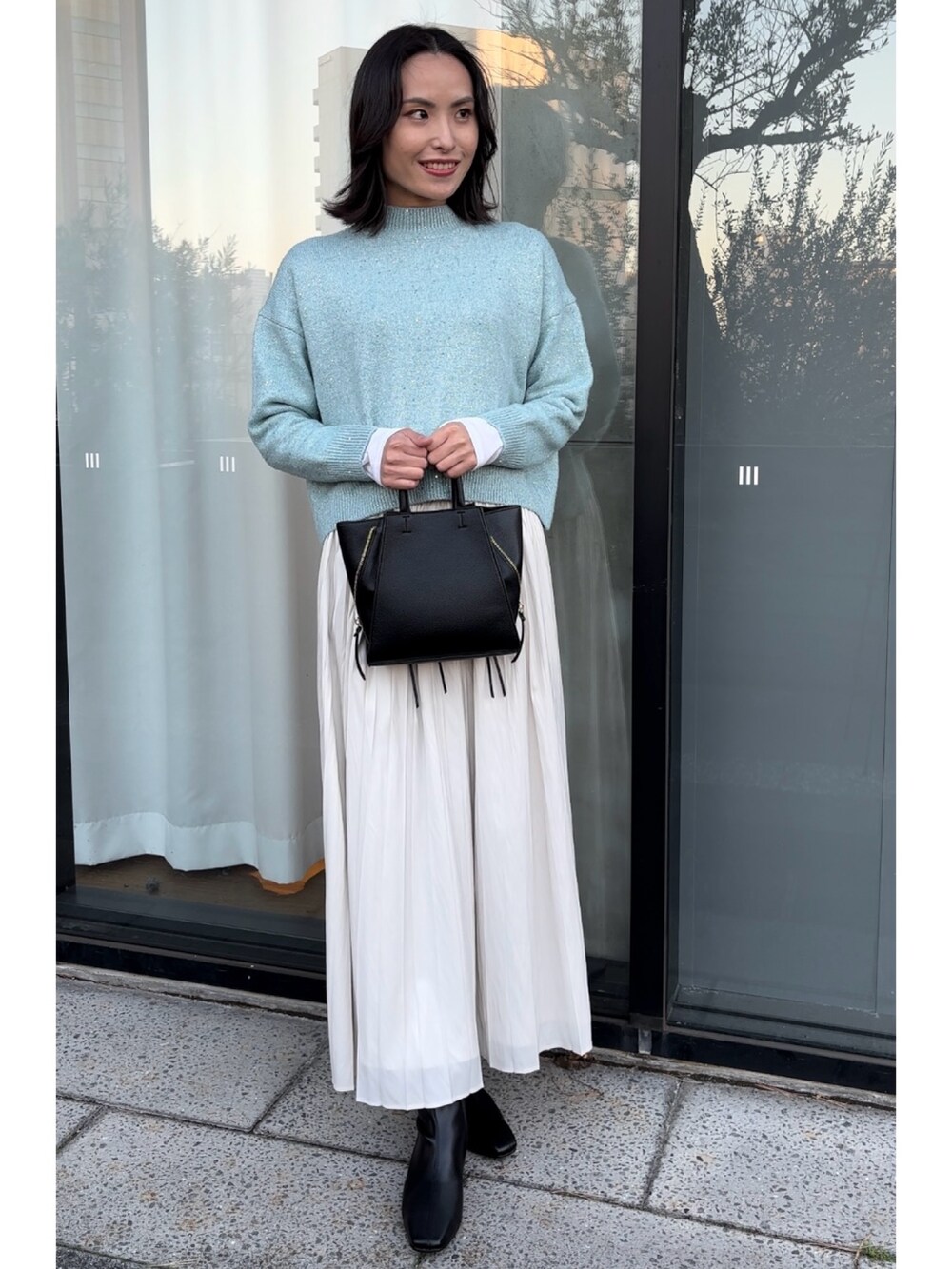 ブルー系のニット/セーター、ブラック系のショルダーバッグ、ホワイト系のスカートを着用したレディースの秋コーディネートの3枚目の写真
