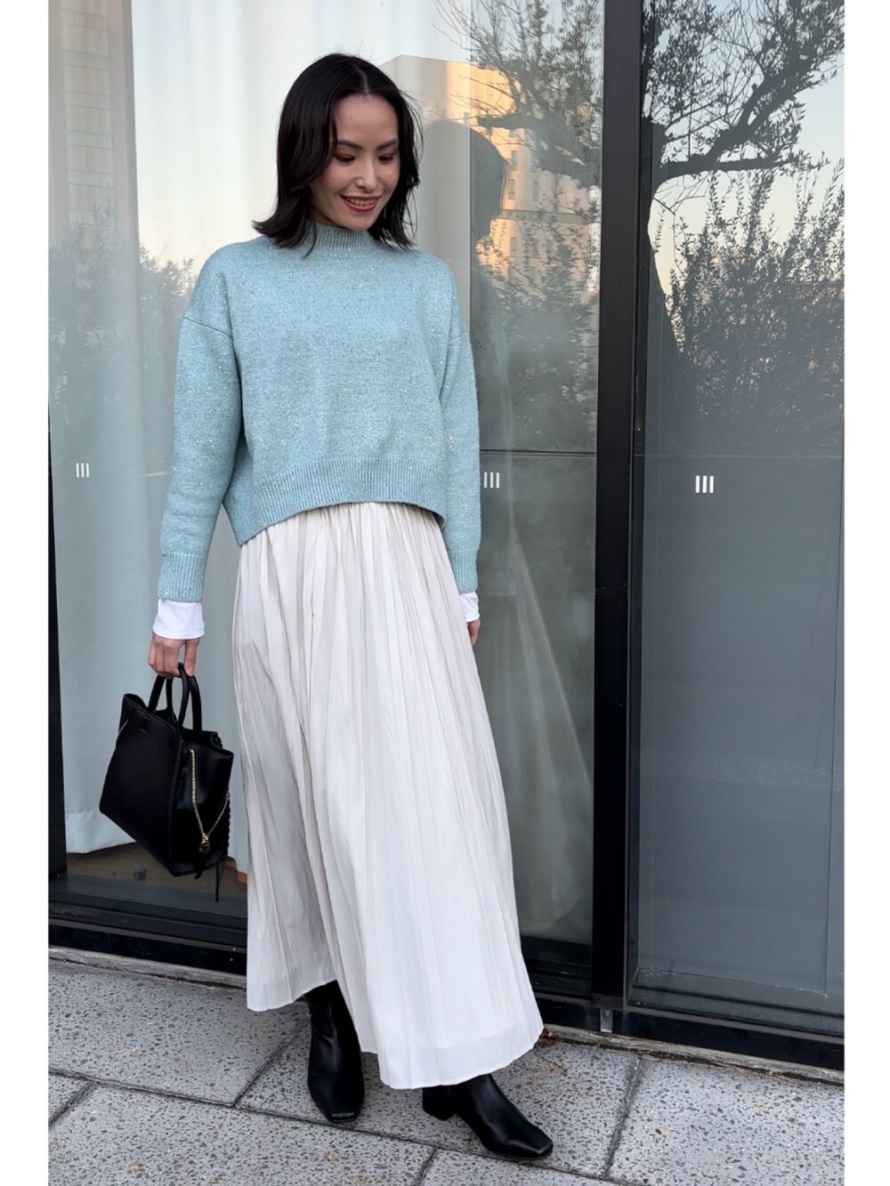 ブルー系のニット/セーター、ブラック系のショルダーバッグ、ホワイト系のスカートを着用したレディースの秋コーディネートの2枚目の写真