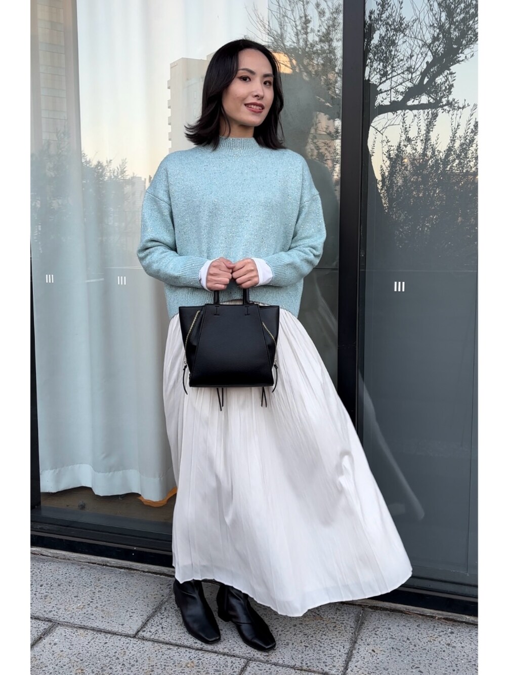 ブルー系のニット/セーター、ブラック系のショルダーバッグ、ホワイト系のスカートを着用したレディースの秋コーディネートの4枚目の写真